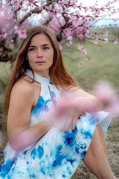 Young beautiful woman in blue dress and long hair is enjoying with blossoming peach trees.