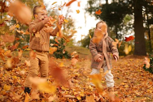 Outdoor fun in autumn. Children playing with autumn fallen leaves in park. Happy little friends