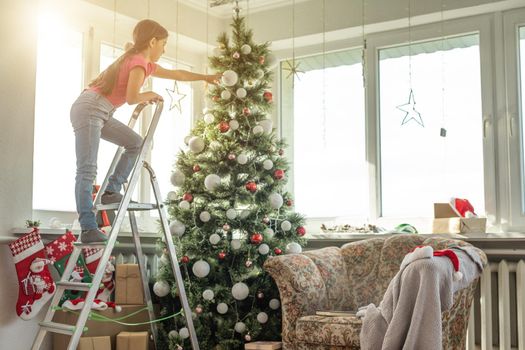 little girl on a stepladder decorating Christmas tree.