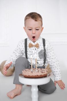 Cute little boy celebrating birthday. Child blowing candles on the birthday cake. Celebration, white minimalist interior