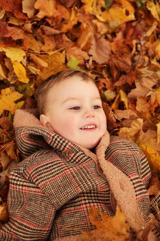 Outdoor fun in autumn. Child playing with autumn fallen leaves in park. Happy little boy lying down on yellow leaves outdoors. View from above
