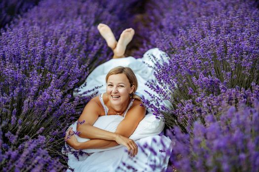 A middle-aged woman lies in a lavender field and enjoys aromatherapy. Aromatherapy concept, lavender oil, photo session in lavender.