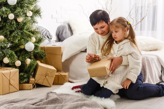holidays, celebration, family and people concept - happy mother and little girl with gift box over living room and christmas tree background.
