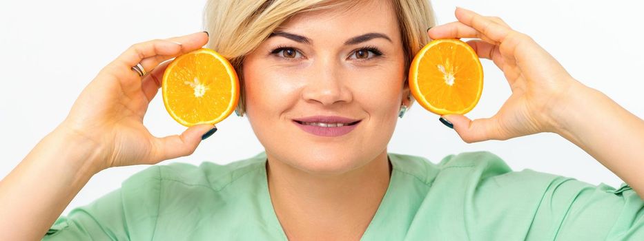 Portrait of young smiling blonde woman cosmetologist with halves of oranges on white background