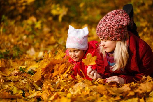 Mother and daughter having fun in the autumn park among the falling leaves