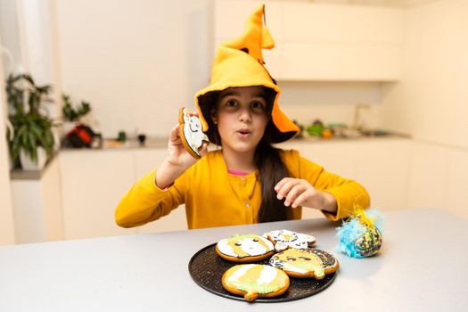 Little girl in Halloween costume plays with gingerbread cookies like a pumpkin.