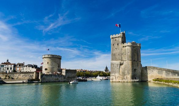 View of the entrance to the old port of the French city of La Rochelle with the two medieval towers and blue sky with light clouds.