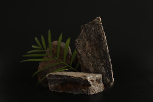 Rock podium on the black background with tropical leaves. Stone podest for product, cosmetic presentation. Creative mock up. Pedestal or platform for beauty products