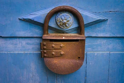 Close-up photograph of a blue-painted wooden door with an antique rusted metal padlock.