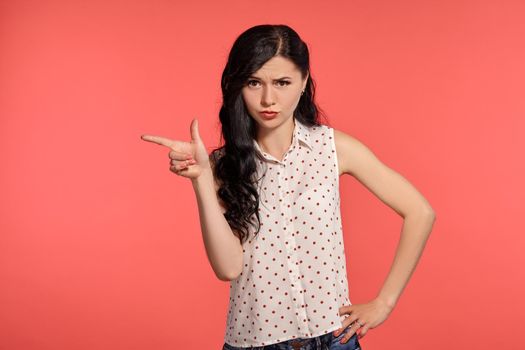 Studio shot of a graceful teeny girl, wearing casual white polka dot blouse. Little brunette female gesticulating posing over a pink background. People and sincere emotions.