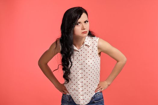 Studio shot of a good-looking little woman, wearing casual white polka dot blouse. Little brunette female is acting like suspect someone, posing over a pink background. People and sincere emotions.