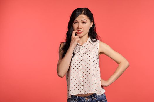 Studio shot of a magnificent teeny girl looking sly, wearing casual white polka dot blouse. Little brunette female is posing over a pink background. People and sincere emotions.