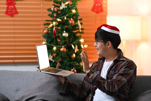 Young man in red Santa hat having video call on laptop computer with his family at Christmas time.