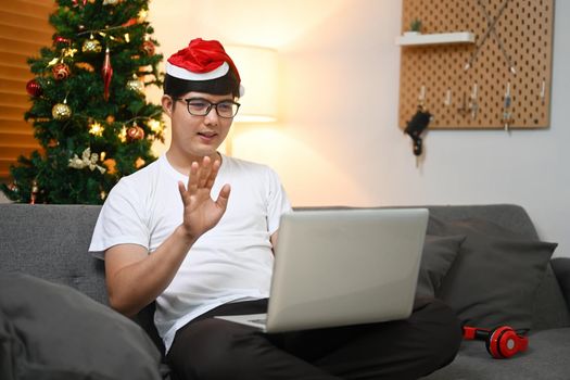 Young man wearing red Santa hat greeting his family during video call at Christmas time