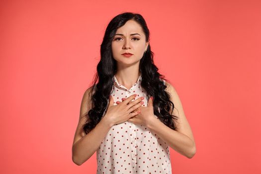 Studio shot of a nice adolescent girl looking at the camera, wearing casual white polka dot blouse. Little brunette female crossed her arms, posing over a pink background. People and sincere emotions.