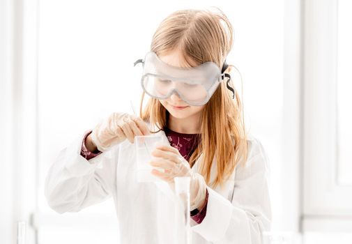 Girl doing scientific chemistry experiment wearing protection glasses. Schoolgirl with equipment and chemical liquids on school lesson