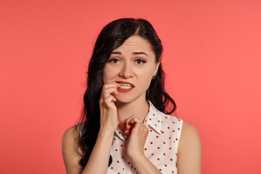 Close-up studio shot of a pretty little woman, wearing casual white polka dot blouse. Little brunette female looking confused, posing over a pink background. People and sincere emotions.