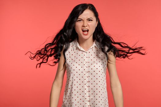 Studio shot of a beautiful screaming teen lady, wearing casual white polka dot blouse. Little brunette female feeling unhappy, posing over a pink background. People and sincere emotions.