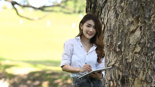 Beautiful Asian woman standing in the park and holding tablet.