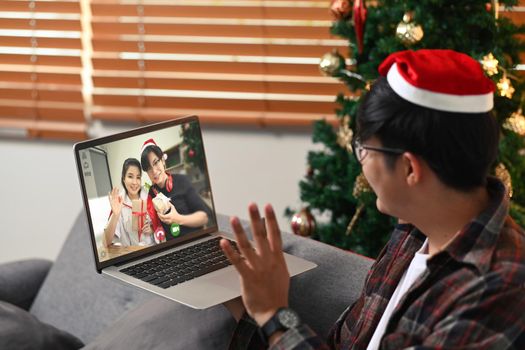 Young man wearing red Santa hat and having video call on laptop computer with his friends.