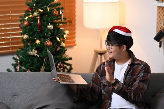 Young asian man in Santa hat greeting his family on laptop for celebrating holiday together.