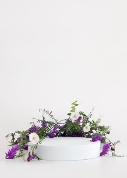 White podium on the white background with flowers. Podium for product, cosmetic presentation. Creative mock up. Pedestal or platform for beauty products. Minimalist design, vertical view.