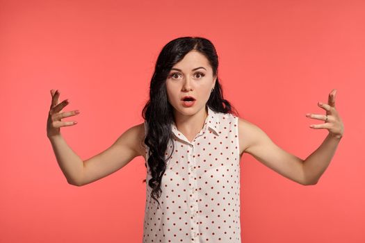 Studio shot of an alluring little woman looking wondered, wearing casual white polka dot blouse. Little brunette is posing over a pink background. People and sincere emotions.