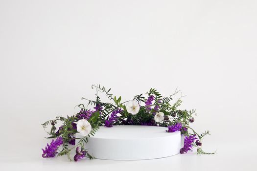 White podium on the white background with flowers. Podium for product, cosmetic presentation. Creative mock up. Pedestal or platform for beauty products. Minimalist design, horizontal view.