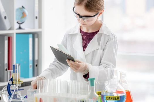 Girl during scientific chemistry experiment making notes close to table with tubes. Schoolgirl with chemical equipment on school lesson