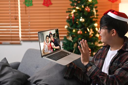 Young Asian man in Santa hat greeting his friends on laptop for celebrating holiday together.