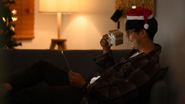 Cheerful asian man wearing Santa hat and having video call with his family on laptop for celebrating holiday together.