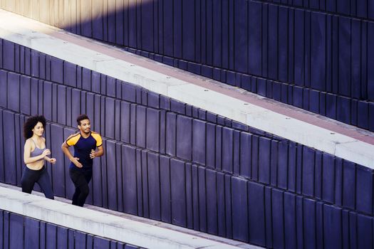 sports woman and man jogging on the city street in modern environment of walls. fitness, urban sports workout and healthy lifestyle concept, copy space for text