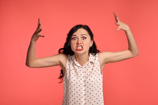 Studio shot of an adorable little woman looking angry, wearing casual white polka dot blouse. Little brunette female feeling unhappy, posing over a pink background. People and sincere emotions.