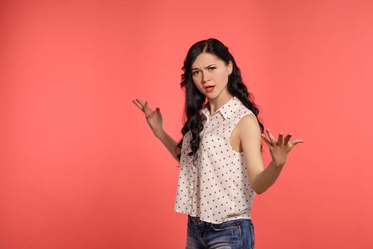 Studio shot of a lovely girl teenager looking upset, wearing casual white polka dot blouse and denim short shorts. Little brunette female feeling unhappy, posing over a pink background. People and sincere emotions.