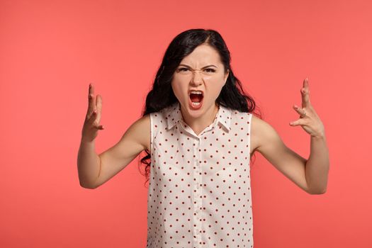 Studio shot of a beautiful screaming little woman, wearing casual white polka dot blouse. Little brunette female feeling disappointed, posing over a pink background. People and sincere emotions.