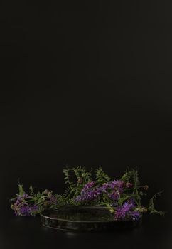 Black podium on the black background with flowers. Podium for product, cosmetic presentation. Creative mock up. Pedestal or platform for beauty products. Minimalist design, vertical view.