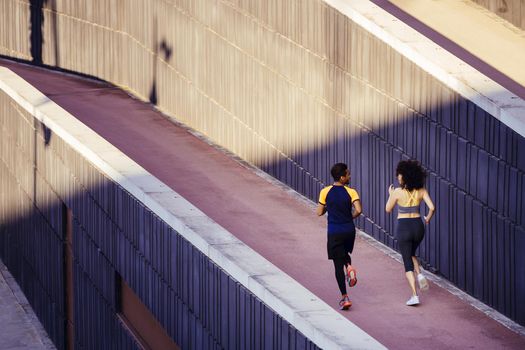 rear view of an interracial couple of runners jogging on the city street in modern environment of walls. fitness, urban sports workout and healthy lifestyle concept, copy space for text