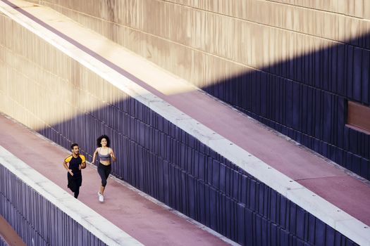 happy young woman and sports man running on the city street in modern environment of walls. fitness, urban sports workout and healthy lifestyle concept, copy space for text