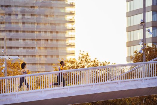 athletic sporty friends running together at sunset in the city bridge with buildings in the background. urban sports workout in couple and healthy lifestyle concept