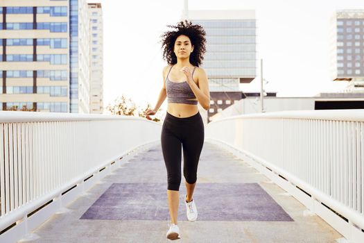 beautiful latin woman running in a city bridge with buildings in the background. urban sports workout and healthy lifestyle concept