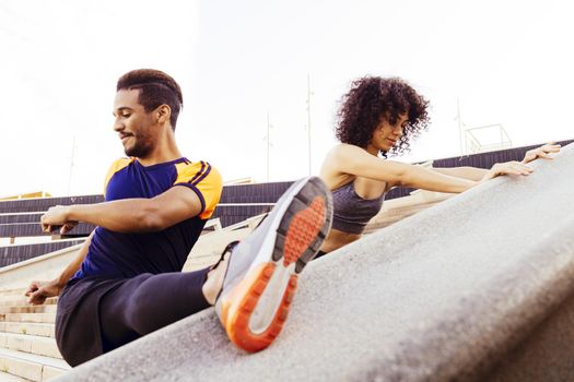 interracial couple of young runners stretching on city stairs before running, fitness, urban sports workout and healthy lifestyle concept, copy space for text