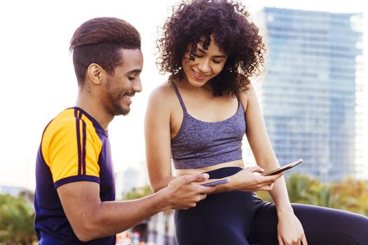 portrait of a athletic latin woman and black man using their mobile phones during a rest in the workout, technology in sport and healthy lifestyle concept