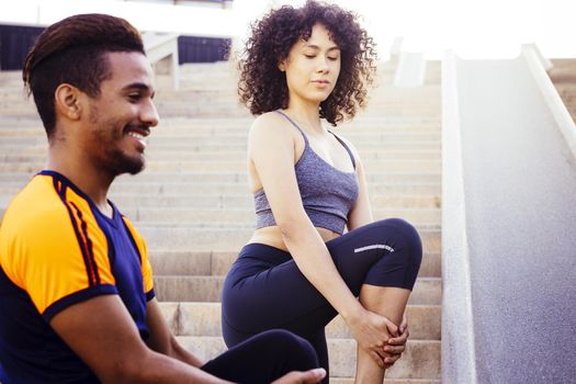 young latin woman and afro american man stretching on city stairs before running. fitness, urban sports workout and healthy lifestyle concept, copy space for text