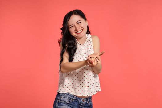 Studio shot of an alluring teen lady wearing casual white polka dot blouse and denim short shorts. Little brunette female is smiling and looking shy posing over a pink background. People and sincere emotions.