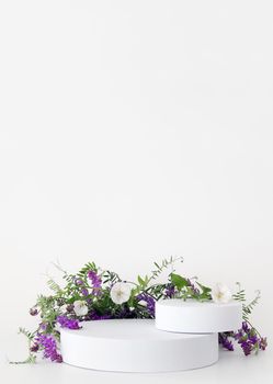 White podium on the white background with flowers. Podium for product, cosmetic presentation. Creative mock up. Pedestal or platform for beauty products. Minimalist design, vertical view.