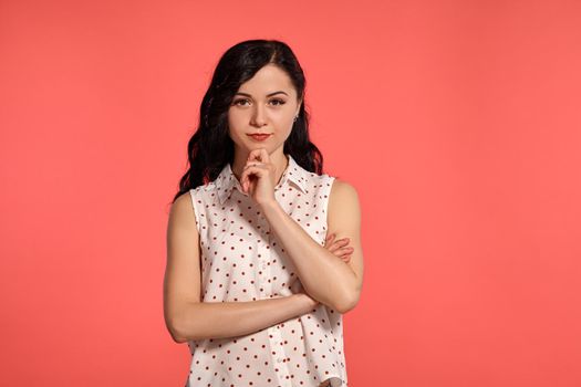 Studio shot of an attractive adolescent girl looking thoughtful, wearing casual white polka dot blouse. Little brunette female posing over a pink background. People and sincere emotions.