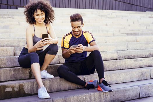 athletic interracial young couple having fun with mobile phone on the stairs during a rest in the workout, technology in sport and healthy lifestyle concept