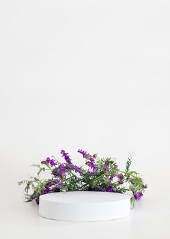 White podium on the white background with flowers. Podium for product, cosmetic presentation. Creative mock up. Pedestal or platform for beauty products. Minimalist design, vertical view.