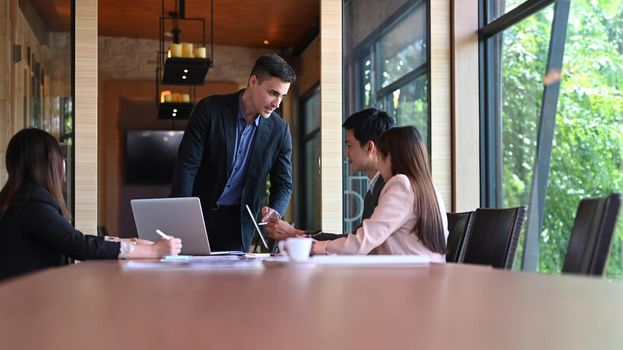 Businesspeople brainstorming and discussing company financial paperwork together in boardroom.