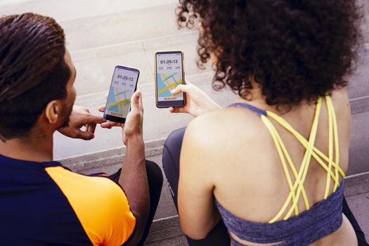 rear view of a interracial athletic young couple looking the sports app in their mobile phones on the stairs during a rest in the workout, technology in sport and healthy lifestyle concept